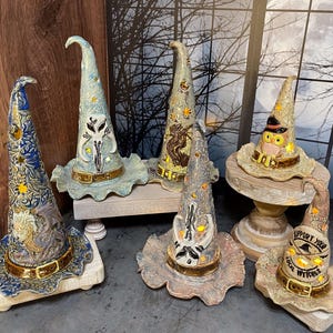 May include: A collection of decorative witch hats in various colors and designs. Each hat features intricate details, including embossed patterns, belt-like bands, and illuminated elements. Some hats have owl or skull motifs.