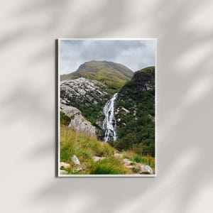 May include: A scenic photograph of a waterfall cascading down a rocky mountainside. Lush green vegetation surrounds the waterfall, with a cloudy sky above.