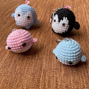 Puede incluir: Cuatro llaveros de pingüino de crochet en diferentes colores: azul, negro, rosa y azul claro. Cada llavero tiene una cara blanca con ojos negros y una pequeña nariz rosa.