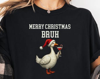 May include: Black t-shirt with the text "MERRY CHRISTMAS BRUH". The graphic features a white goose wearing a Santa hat and holding a cocktail. The goose has orange feet and a red beak. The shirt is a crew neck.