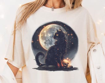 May include: Ivory-colored t-shirt featuring a black cat illustration with a full moon and skull. The cat is sitting in front of a glowing moon with stars. The word "Ivory" is printed at the top left.