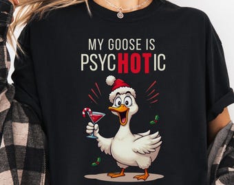 May include: Black graphic t-shirt featuring a cartoon goose wearing a Santa hat and holding a cocktail. The text "MY GOOSE IS PSYCHOTIC" is printed above the goose. A fun and festive design for the holiday season.