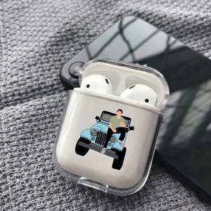 Puede incluir: Una funda protectora transparente para auriculares inalámbricos con un estampado gráfico de una persona con camiseta verde sentada sobre el capó de un vehículo todoterreno azul claro. La funda está abierta y muestra auriculares blancos.