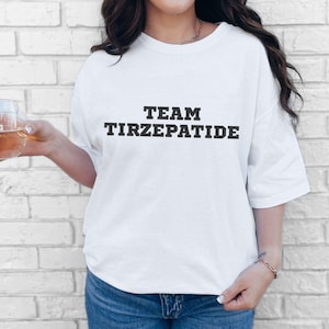 May include: White t-shirt with black text that reads "TEAM TIRZEPATIDE".