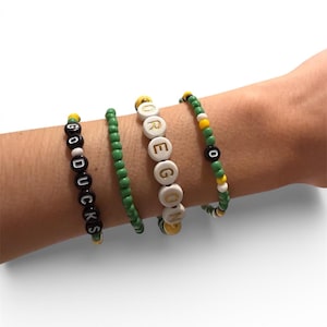 May include: Four beaded bracelets in green, white, black, and yellow. One bracelet spells "GO DUCKS" in black letters on white beads. Another spells "OREGON" in white letters on black beads. The other two bracelets have solid beads.