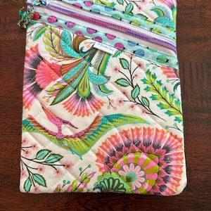 May include: Quilted fabric pouch with a vibrant floral and bird pattern in pink, green, and teal. The pouch has two zippered compartments with a light blue and pink zipper. The fabric is quilted with a diamond pattern.