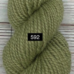 May include: Close-up of a skein of olive green yarn. The yarn is thick and textured, with visible fibers. A small black rectangle with the number "592" is visible on the yarn. The yarn is likely for knitting or crocheting projects.
