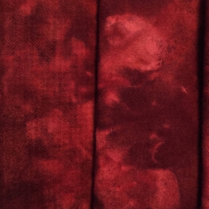 May include: Four fabric swatches in different shades of red. The swatches are arranged side-by-side. The fabric on the left has a plaid pattern. The other three fabrics have a mottled, tie-dye effect.
