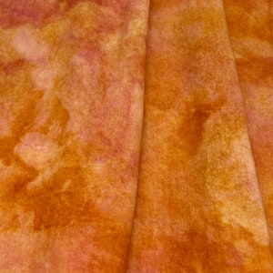 May include: A close-up of a fabric with a tie-dye pattern in shades of orange, yellow, and pink. The fabric is folded in half, and the folds create a soft, textured look.