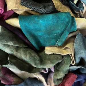 May include: A pile of colorful fabric scraps in various shades of green, blue, purple, and brown. The fabric is soft and textured, and it appears to be made of wool or cotton.