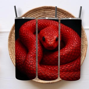 May include: Three black tumblers featuring a red snake design. The snake is coiled and has a textured appearance. The tumblers have black straws and are set in a woven basket.