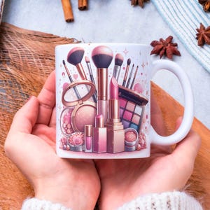 Può includere: Tazza in ceramica bianca con un design di trucco rosa e oro rosa. Il design include pennelli per il trucco, rossetto, ombretto e ciprie. La tazza ha un manico bianco.