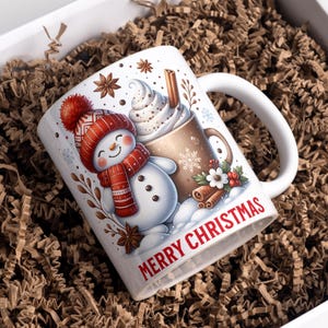 Peut inclure: Mug en céramique blanche avec un motif de Noël festif. La tasse représente un bonhomme de neige portant un chapeau et une écharpe rouges, et une tasse de chocolat chaud avec de la crème fouettée. L'inscription "MERRY CHRISTMAS" est en rouge.