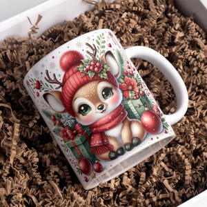 May include: White ceramic mug with a cartoon deer wearing a red hat and scarf, decorated with Christmas ornaments and gifts. The mug has a white handle and is presented in a box with brown paper filler.
