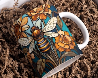 May include: White ceramic mug featuring a detailed illustration of a bee with orange and yellow flowers against a teal background. The bee has brown and black stripes. The mug has a white handle.