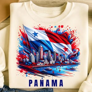 May include: Cream-colored sweatshirt featuring a vibrant graphic of the Panama flag waving over a cityscape. The design incorporates red, white, and blue colors with the word "PANAMA" at the bottom. The image includes a skyline and boats on the water.