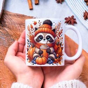 Könnte beinhalten: Weiße Keramiktasse mit einem Cartoon-Waschbären, der einen orangefarbenen Hut und Schal trägt und ein Getränk hält. Die Tasse ist mit Kürbissen, Beeren und Herbstblättern verziert. Die Tasse wird in zwei Händen gehalten.