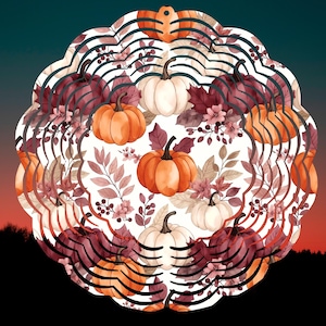 Op de afbeelding: Een ronde metalen windspinner met een herhalend patroon van oranje en witte pompoenen, donkerrode herfstbladeren en kleine bessen. Het ontwerp is gedrukt op een witte achtergrond met een geschulpte rand en een ophanggat aan de bovenzijde.