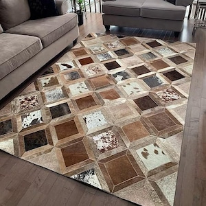 Puede incluir: Una alfombra rectangular con un diseño geométrico de patchwork compuesto por baldosas cuadradas. La alfombra muestra una variedad de texturas de piel de vaca natural en tonos marrón, beige, blanco y negro, dispuestas en un patrón de cuadrícula.