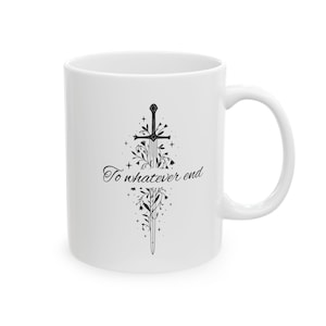 May include: White ceramic mug featuring a black sword design with floral accents and the text "To whatever end." The mug has a curved handle and a glossy finish, suitable for hot or cold beverages.