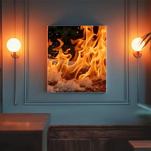 Könnte beinhalten: Ein gerahmter Druck von Flammen in Orange- und Gelbtönen mit einer strukturierten weißen Basis. Das Kunstwerk wird an einer grauen Wand ausgestellt, die von warm getönten Wandleuchten beleuchtet wird. Das Thema ist eine feurige, abstrakte Darstellung.