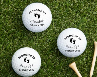 Puede incluir: Tres pelotas de golf blancas con el texto "PROMOTED TO grandpa February 2025" en negro. Las pelotas de golf están sobre hierba verde con dos tees de golf de madera.