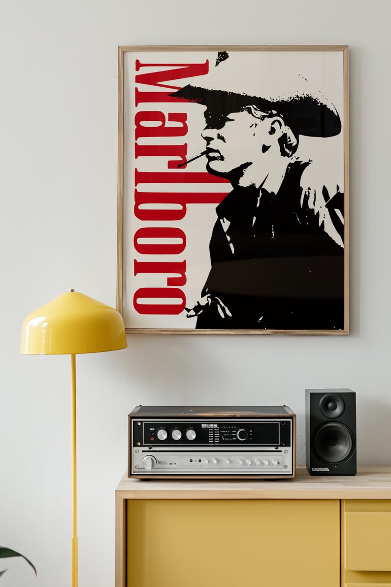Op de afbeelding: Een ingelijste poster met het woord "Marlboro" in het rood en een zwart-wit afbeelding van een rokende cowboy. Een gele lamp en stereo-apparatuur staan op een gele kast. Rechts staat een zwarte luidspreker.