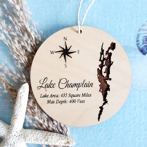 May include: A wooden ornament with a compass and the outline of Lake Champlain. The text reads "Lake Champlain, Lake Area: 435 Square Miles, Max Depth: 400 Feet."
