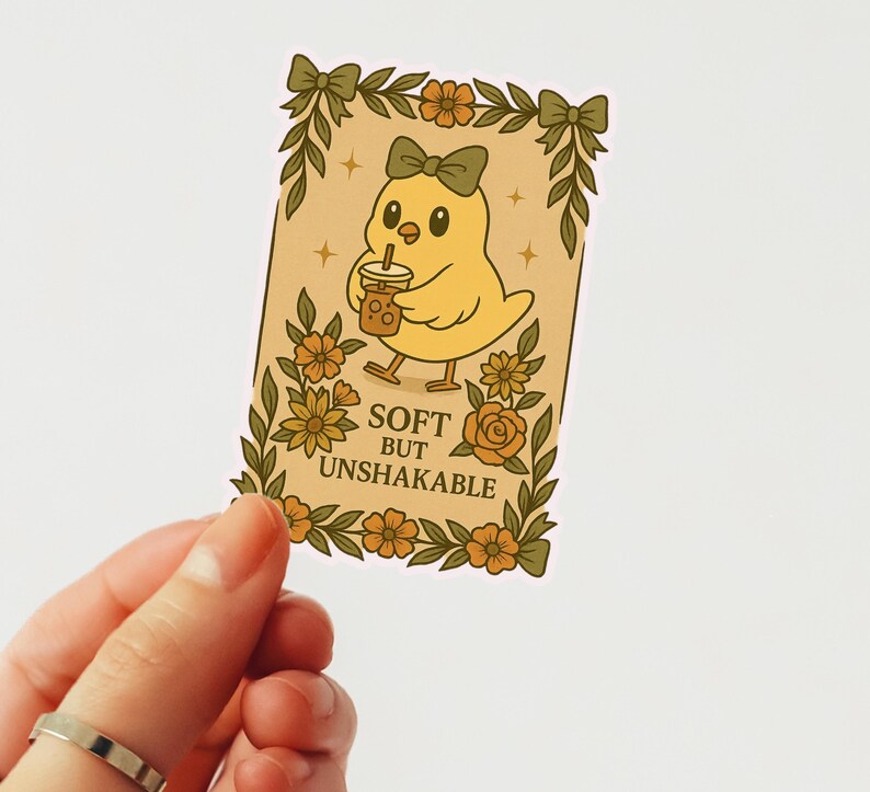 May include: A sticker with a cartoon yellow chick wearing a green bow, holding a drink with a straw. The sticker has a floral border and the text "SOFT BUT UNSHAKABLE".