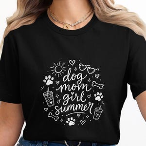 Puede incluir: Camiseta negra con un diseño gráfico blanco que dice "dog mom girl summer" en un círculo. El diseño incluye huellas de patas, corazones, gafas de sol, un sol y una taza de café.