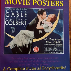 May include: A book titled "Academy Award Winners' Movie Posters" featuring a movie poster from "It Happened One Night" with Clark Gable and Claudette Colbert. The cover is purple with yellow text and a romantic illustration.
