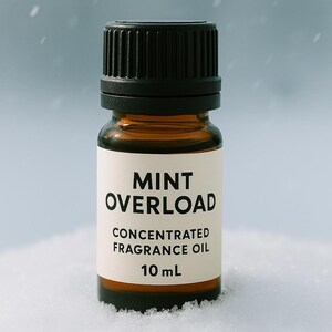 May include: A small amber glass bottle with a black cap, labeled "MINT OVERLOAD CONCENTRATED FRAGRANCE OIL 10 mL." The bottle is set against a snowy background, with falling snowflakes. The label is white with black text.