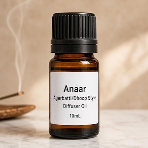 May include: A brown glass bottle with a black cap, labeled "Anaar Agarbbati/Dhoop Style Diffuser Oil 10mL." The bottle is set against a neutral background, with wisps of smoke rising in the background, suggesting the use of incense.