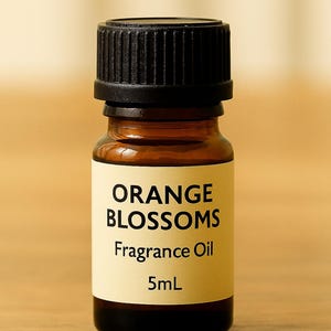May include: A small amber glass bottle with a black cap. The label reads "ORANGE BLOSSOMS Fragrance Oil 5mL". The bottle is filled with a golden liquid, suggesting an essential oil or perfume.