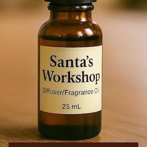 May include: A brown glass bottle with a black cap, labeled "Santa's Workshop Diffuser/Fragrance Oil, 25 mL." The bottle is on a wooden surface. The words "Santa's Workshop" are also displayed in a brown banner.