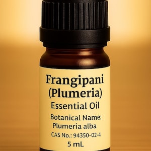 May include: A small, brown glass bottle of Frangipani (Plumeria) Essential Oil with a black cap. The label displays the botanical name, Plumeria alba, and the volume, 5 mL. The background is a warm, golden color.