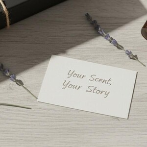 May include: Aromatherapy product arrangement featuring a brown glass bottle, a wooden roller, and sprigs of lavender. A white card with the text "Your Scent, Your Story" is also present. The items are arranged on a light wood-grain surface.