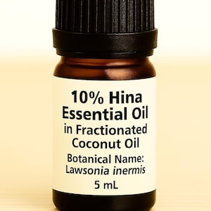 May include: A small brown glass bottle with a black cap, labeled with white text. The label reads "10% Hina Essential Oil in Fractionated Coconut Oil" and "Botanical Name: Lawsonia inermis, 5 mL".