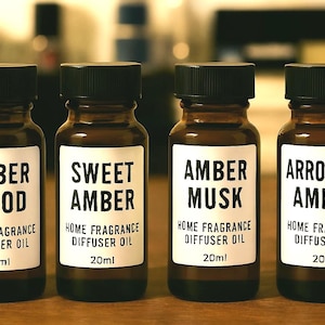 May include: Four amber-colored glass bottles with black caps, each labeled with a different scent: "Amber Wood", "Sweet Amber", "Amber Musk", and "Arrogant Amber". The labels also state "Home Fragrance Diffuser Oil" and "20ml".