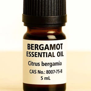 May include: A small amber glass bottle of bergamot essential oil with a black cap. The label reads "BERGAMOT ESSENTIAL OIL Citrus bergamia" and includes the CAS number and 5 mL volume.