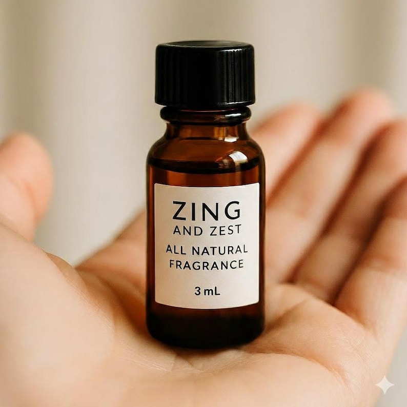 May include: A small amber glass bottle with a black cap, labeled "ZING AND ZEST ALL NATURAL FRAGRANCE" and 3 mL. The bottle is held in an open hand, suggesting a focus on natural fragrance products.