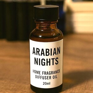 May include: A brown glass bottle with a black cap, labeled "ARABIAN NIGHTS HOME FRAGRANCE DIFFUSER OIL 20ml." The bottle sits on a wooden surface. The label is white with black text.