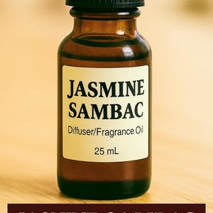 May include: A brown glass bottle with a black cap, labeled "JASMINE SAMBAC Diffuser/Fragrance Oil 25 mL." The text "JASMINE SAMBAC" is also displayed on a dark brown banner at the bottom. The bottle sits on a light brown surface.