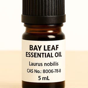 May include: A small amber glass bottle of Bay Leaf Essential Oil with a black cap. The label displays the text "BAY LEAF ESSENTIAL OIL", "Laurus nobilis", and "5 mL". The bottle is on a light wood surface.