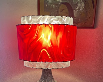 May include: A vintage table lamp with a red and white swirl lampshade and a black and white patterned base. The lamp is sitting on a wooden table.