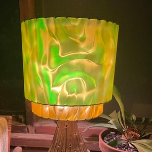 May include: A ceramic table lamp with a green and yellow swirl patterned lampshade. The lamp base has a unique design with multiple holes and a textured surface.