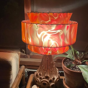 May include: A mid-century modern table lamp with a three-tiered orange and yellow lampshade. The lamp base is brown and has a textured, organic design.