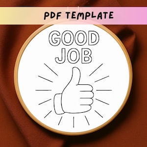 Puede incluir: Un bastidor de bordado blanco con las palabras "GOOD JOB" y una ilustración de pulgar hacia arriba en negro. El texto "PDF TEMPLATE" está en la parte superior. El bastidor tiene un marco de madera y está sobre un fondo marrón.