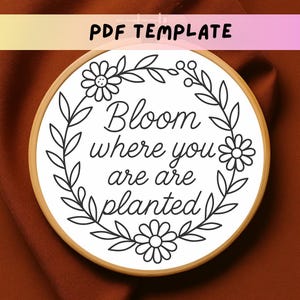 May include: A round embroidery hoop with the text "Bloom where you are planted" surrounded by a floral design. The text and floral elements are black on a white background. The hoop is made of wood, and the words "PDF TEMPLATE" are at the top.