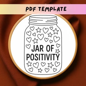 May include: A black and white line drawing of a jar filled with hearts and stars, with the words "JAR OF POSITIVITY" in the center. The jar is set inside a wooden embroidery hoop, with the text "PDF TEMPLATE" at the top.